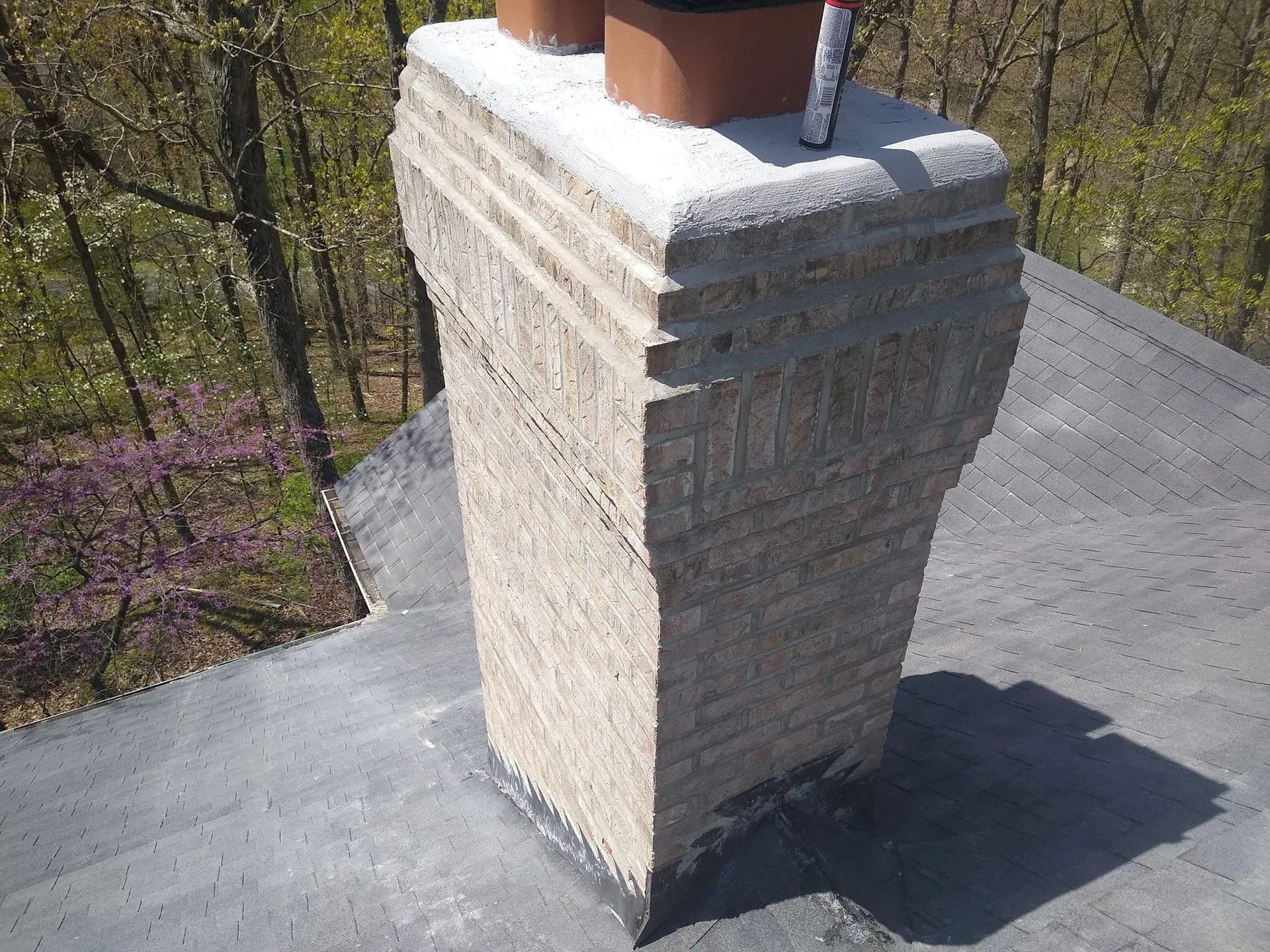 Stone chimney on a rooftop with a terracotta pot, beside a wooded area.
