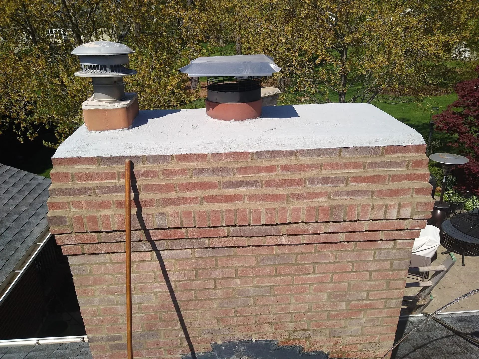 Brick chimney on a roof with two metal vents and white snow on top