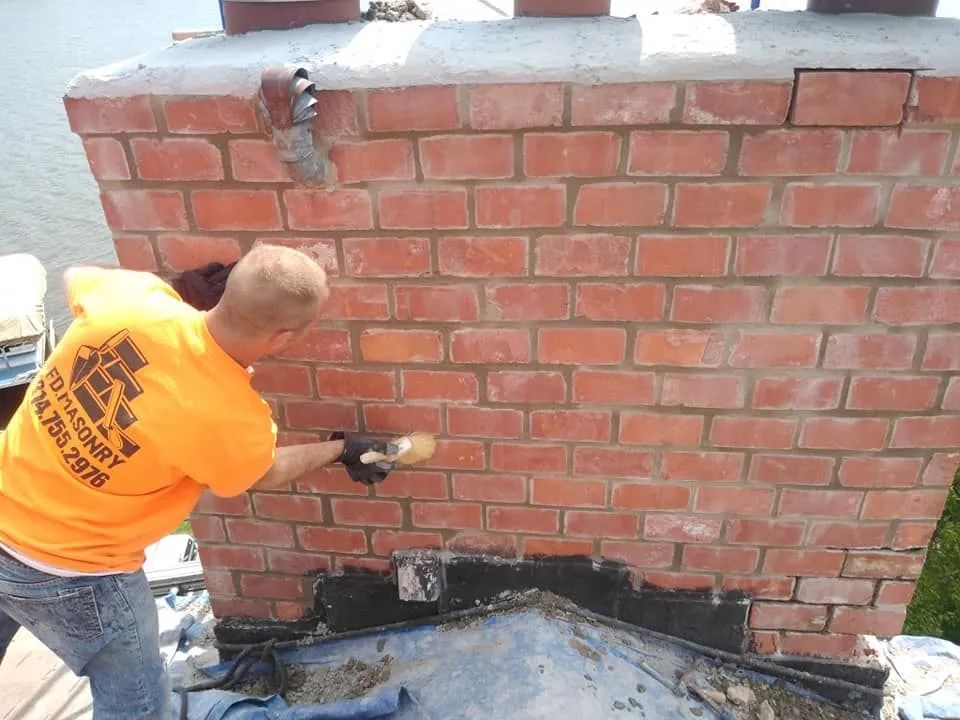 Worker in orange shirt drilling holes in a brick wall outdoors
