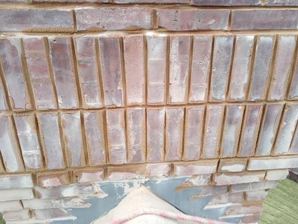 Broken brick wall with cracked mortar and peeling paint at the base