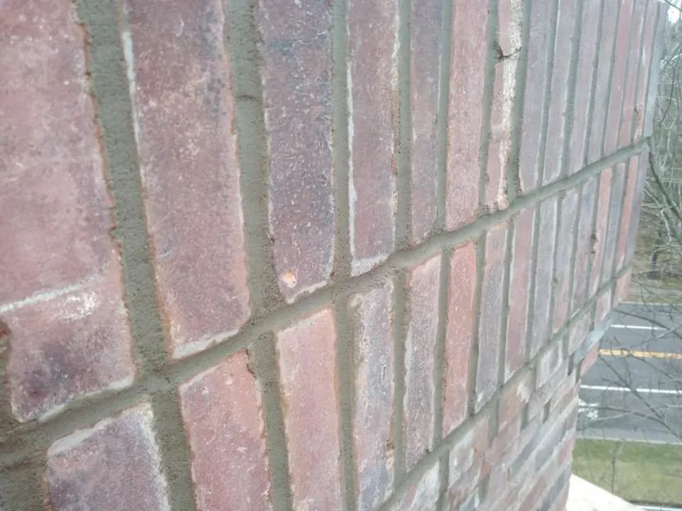 Close-up of a red brick wall with a sidewalk and street in the background.