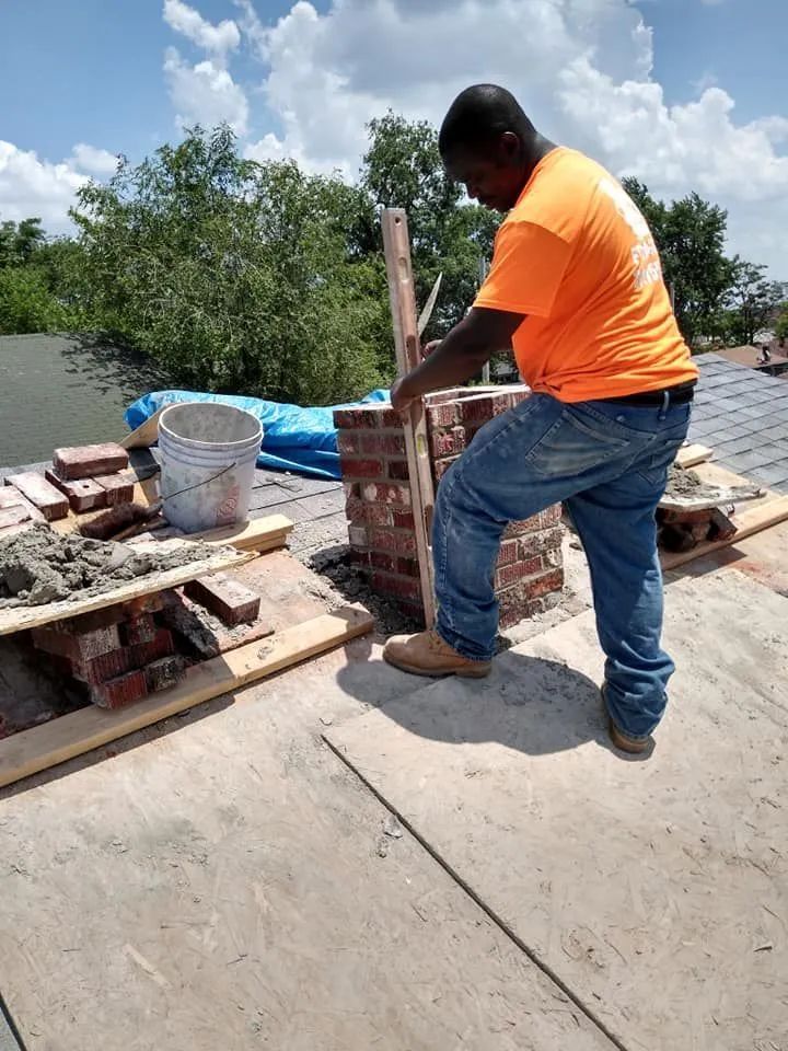 Man in orange shirt and jeans working with bricks and tools on a sunny construction site