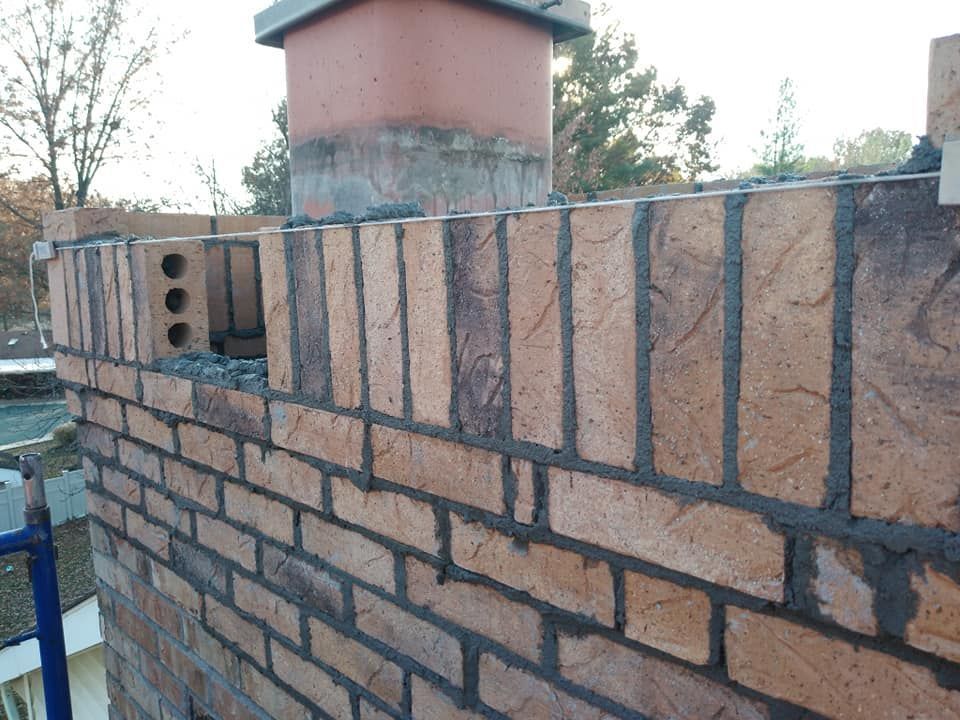 Partially built brick wall with a pink chimney against an outdoor background