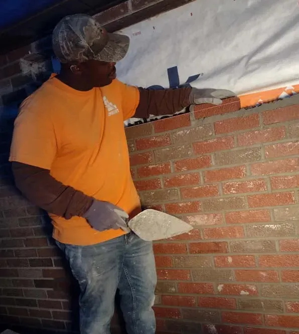 Worker in orange shirt plastering a brick wall under a white tarp cover