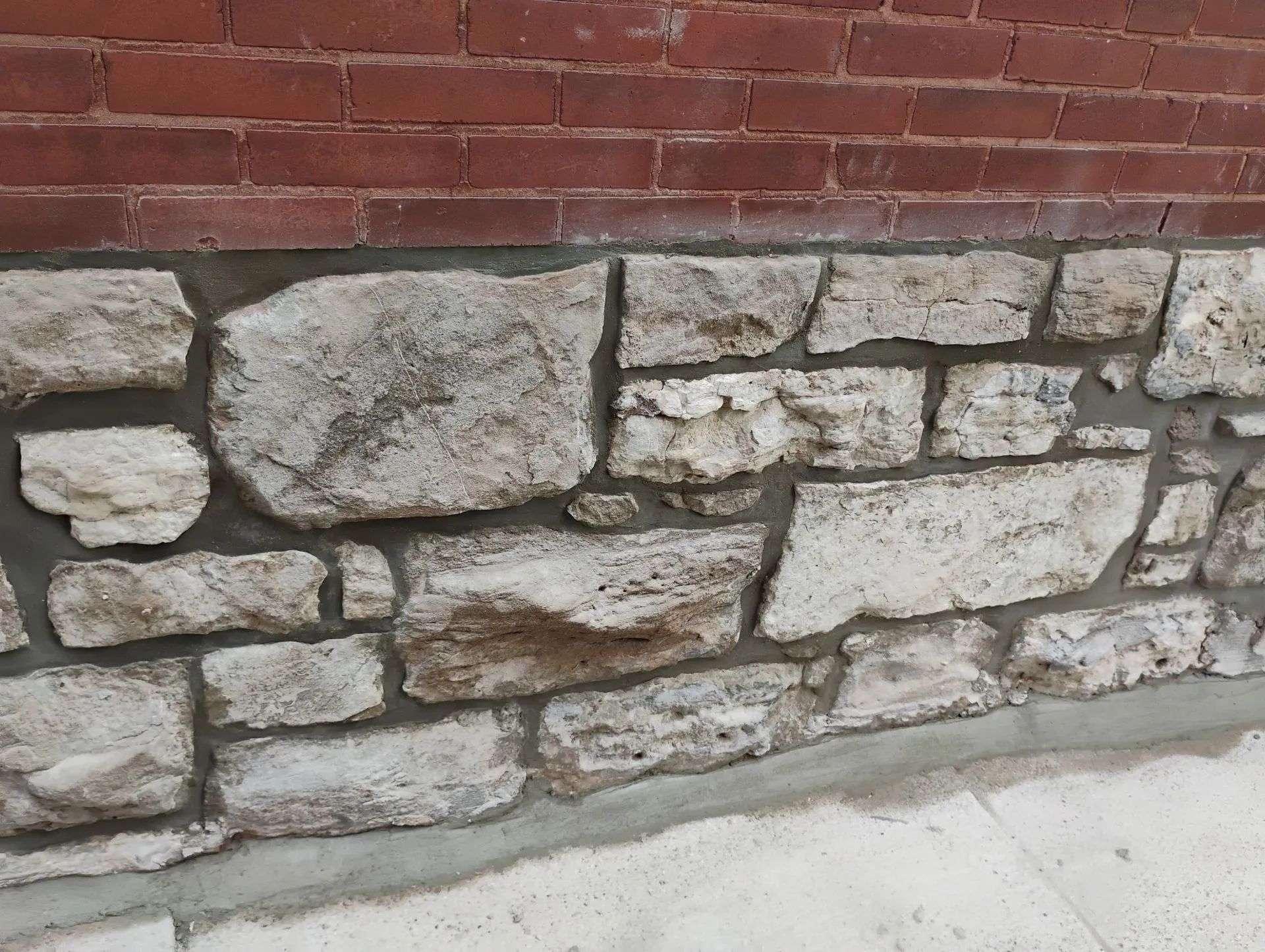 Red brick wall above a gray stone foundation along a concrete walkway.