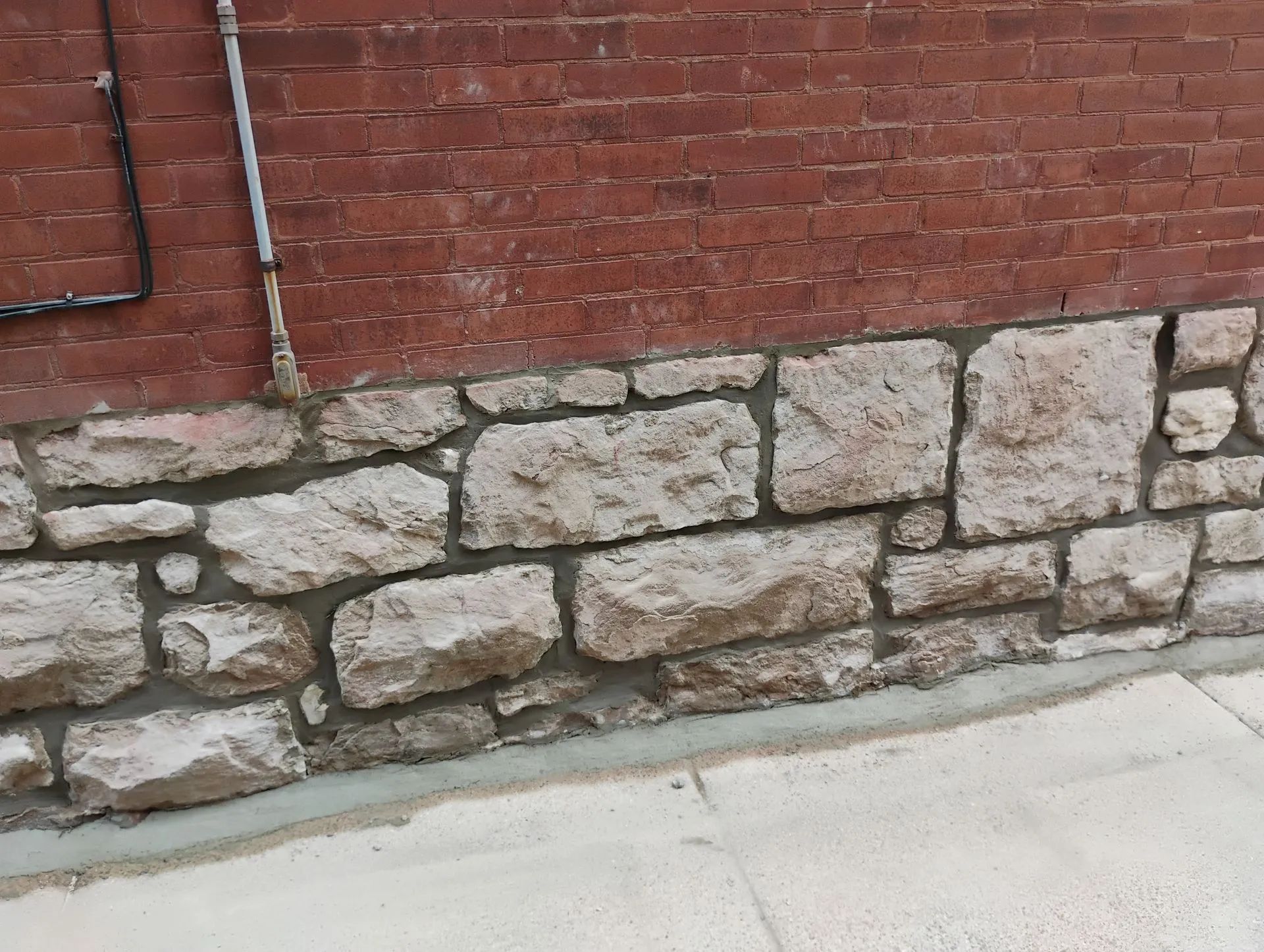 Red brick wall with a stone foundation beside a concrete sidewalk.