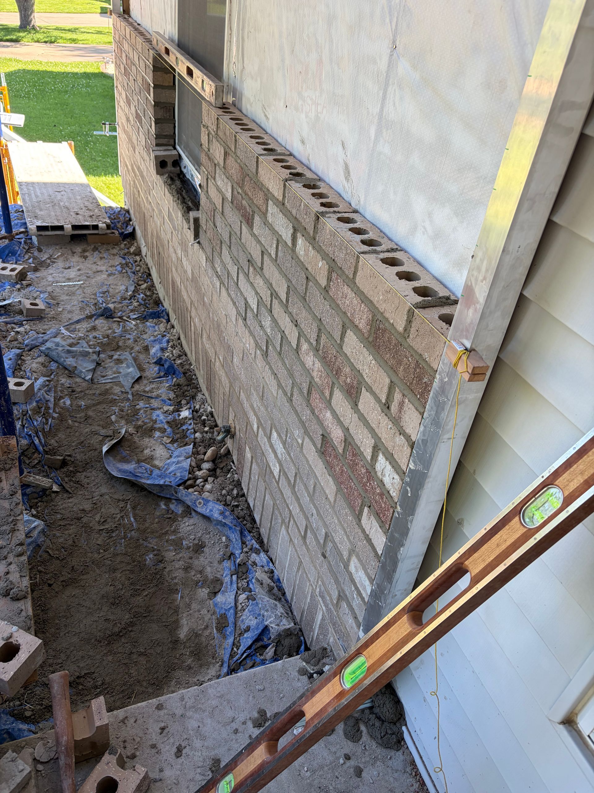 Brick foundation repair beside a house, with a muddy trench and a level leaning against the wall