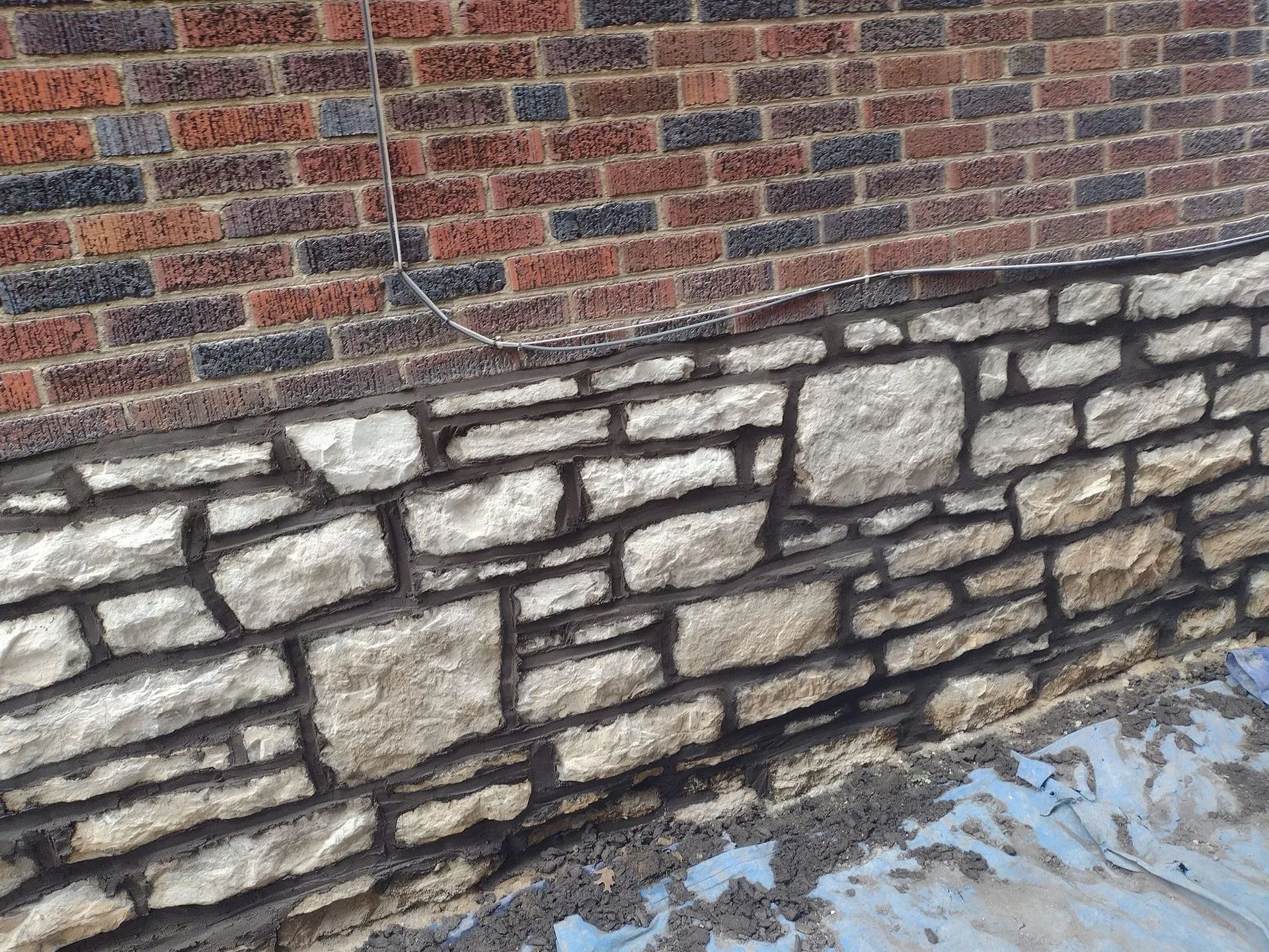 Brick house wall with a stone foundation beside wet ground and snow patches