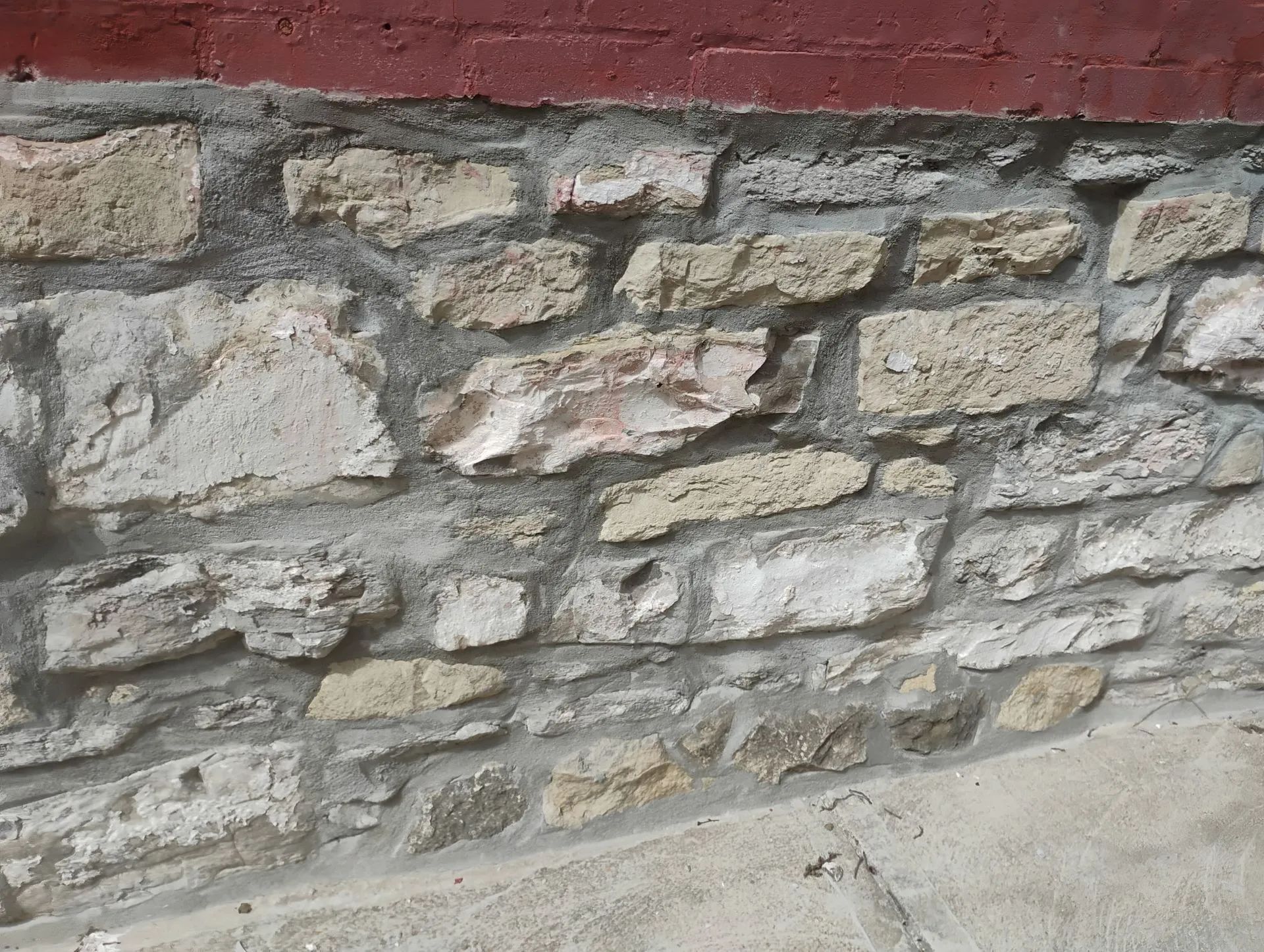 Close-up of a rough stone wall with a red painted top edge beside a concrete sidewalk