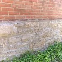 Brick wall over rough stone foundation with green grass at the base