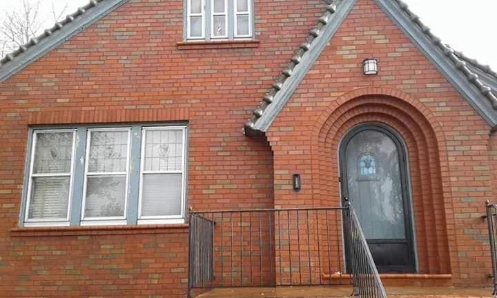 Red brick house with arched front door, white-framed windows, and a small metal railing