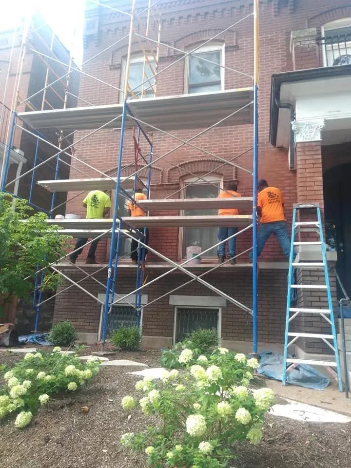 Two workers on scaffolding painting a brick building exterior