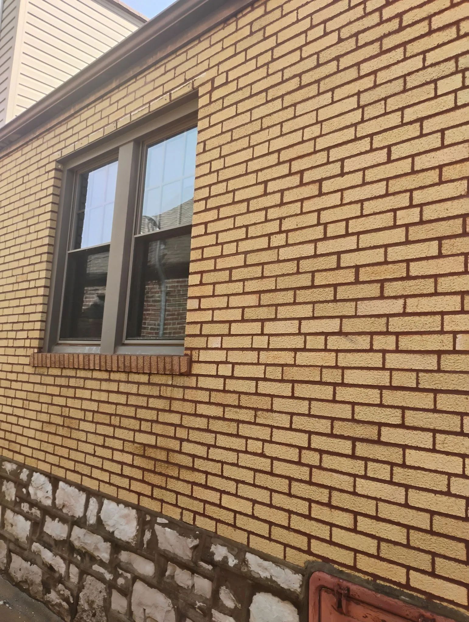 Brick exterior wall with a window and white stone foundation section