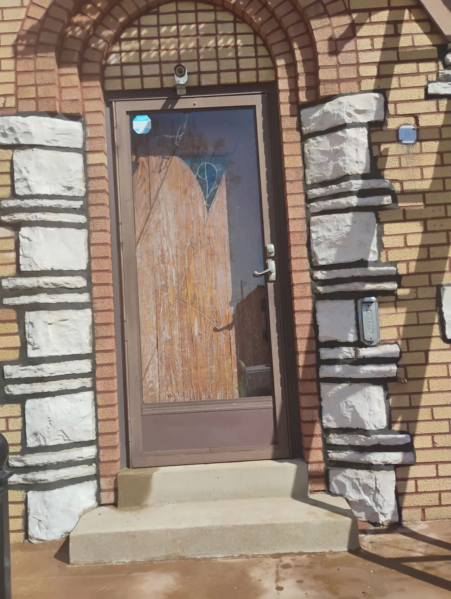 Boarded front door in a stone and brick entryway with concrete steps.