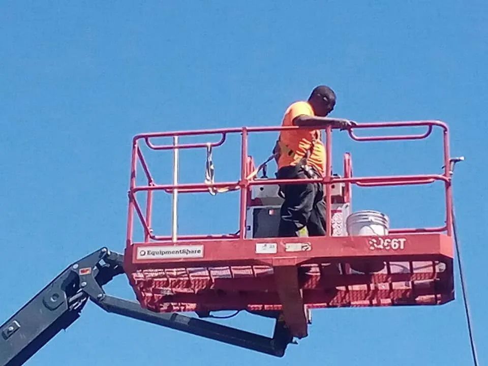 Worker in orange vest standing in a red boom lift against a clear blue sky