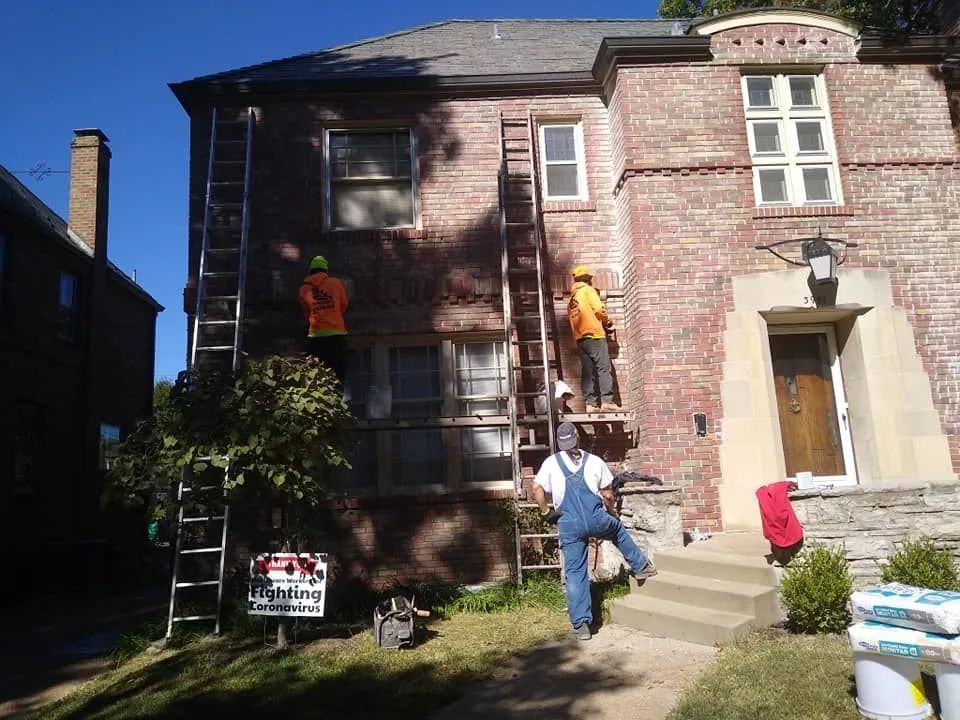 Workers painting a brick house exterior with ladders in a sunny yard