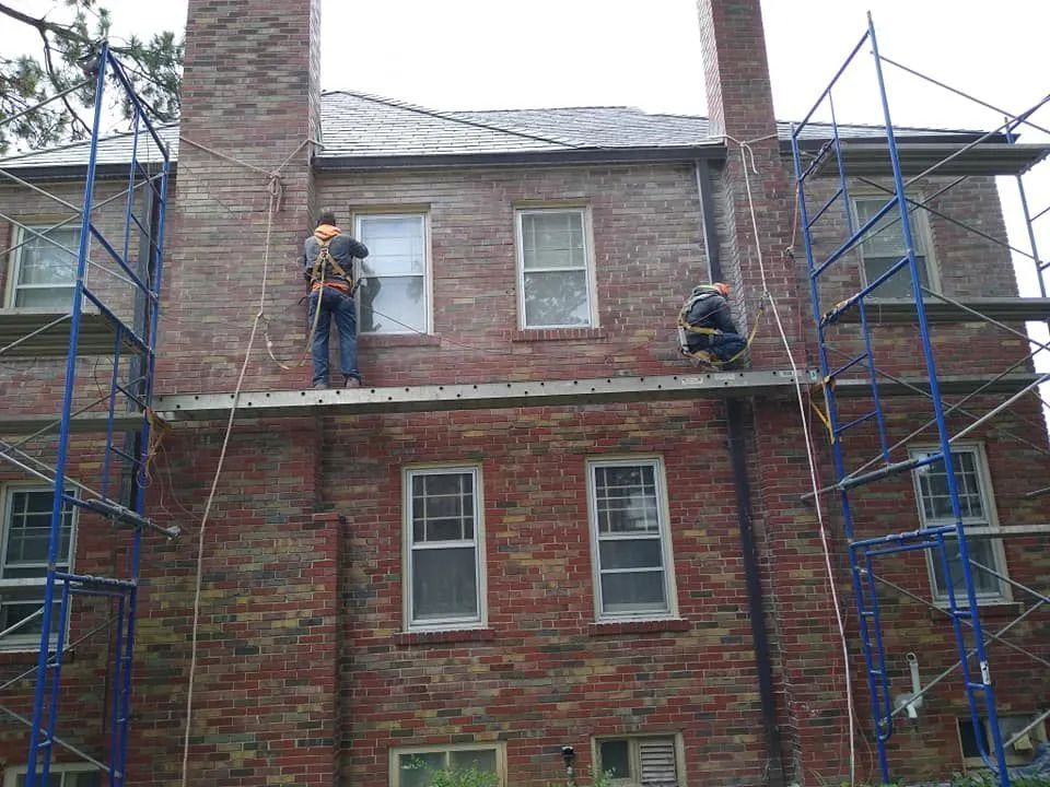 Workers on scaffolding repairing a brick house exterior around windows and roofline