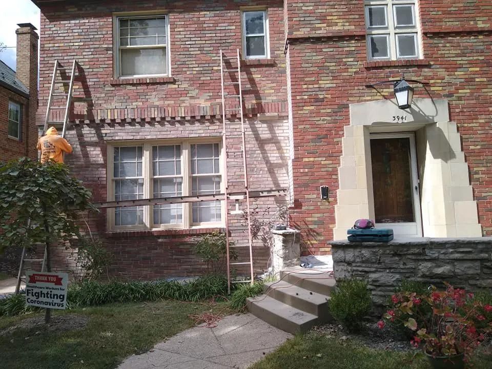 Brick apartment building entrance with steps, white archway, windows, and flower beds.