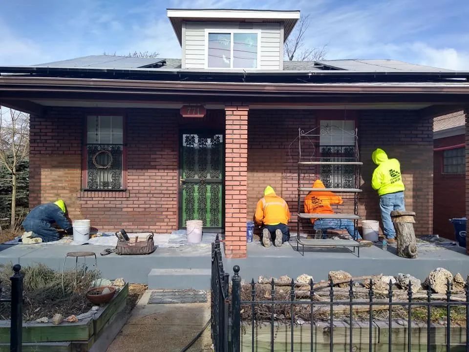 Workers repairing the front porch of a brick house, with tools and materials spread across the steps.
