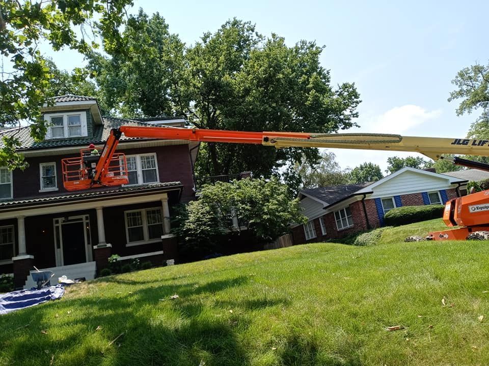 Crane lifting a long orange boom over a house on a grassy residential lawn
