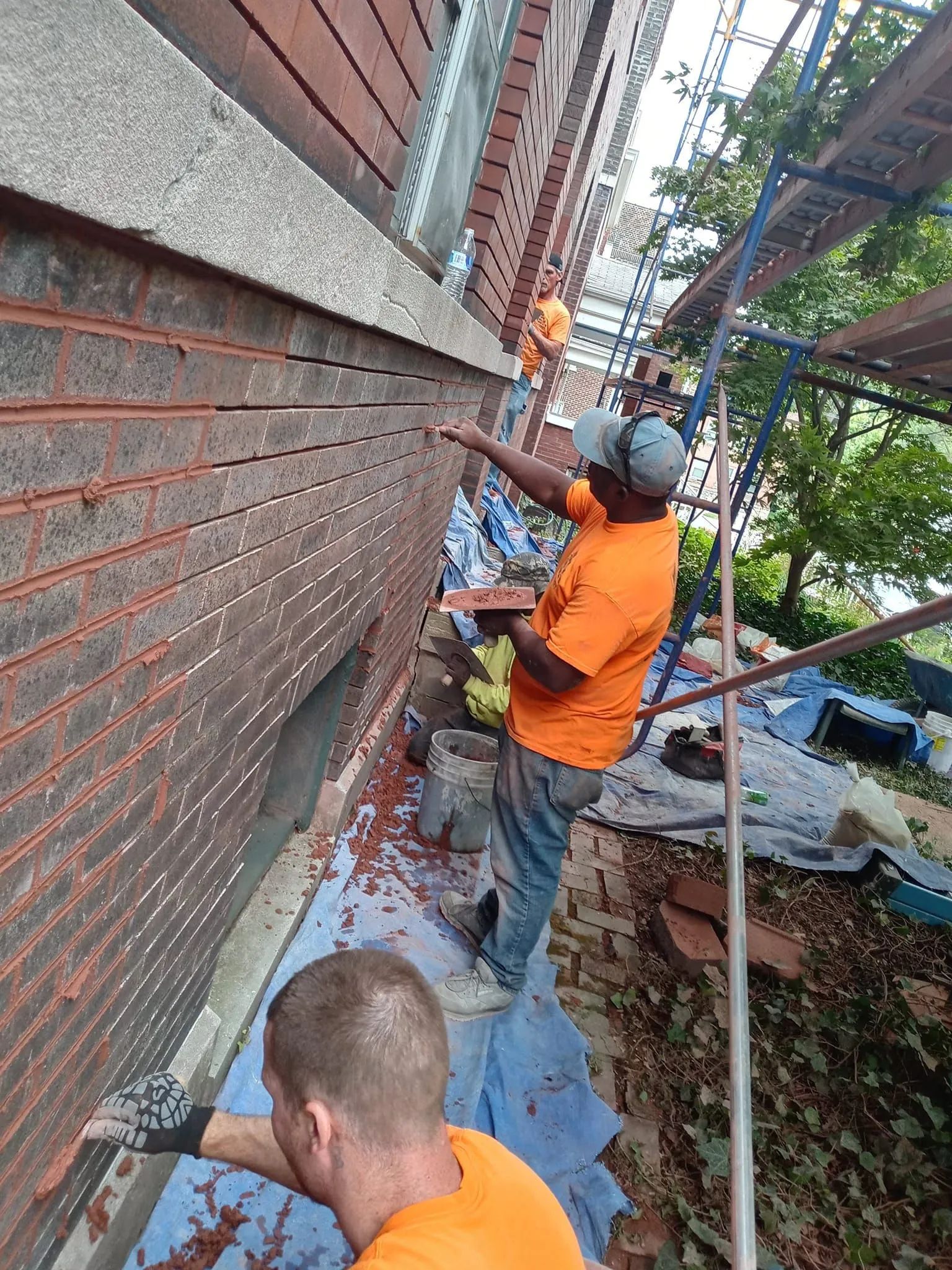 Workers on scaffolding repairing a brick wall, with tools and debris along the building exterior.