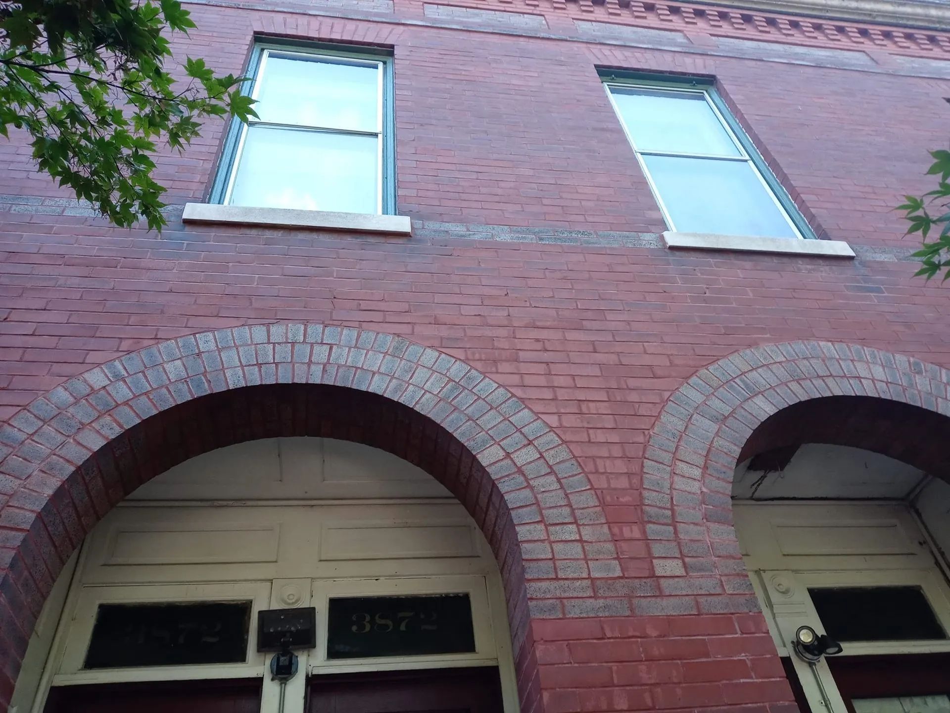 Brick building facade with two arched garage openings and windows above under a tree branch