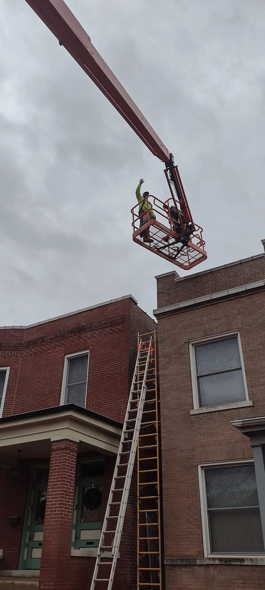 Suspended work platform above brick row houses under a cloudy sky