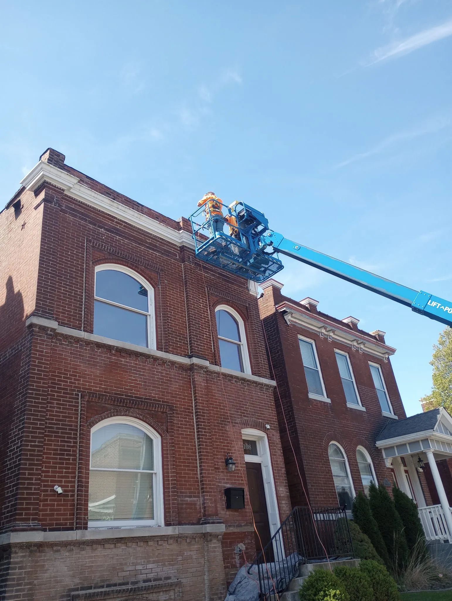 Brick building with arched windows being inspected by a worker in a blue lift against a blue sky