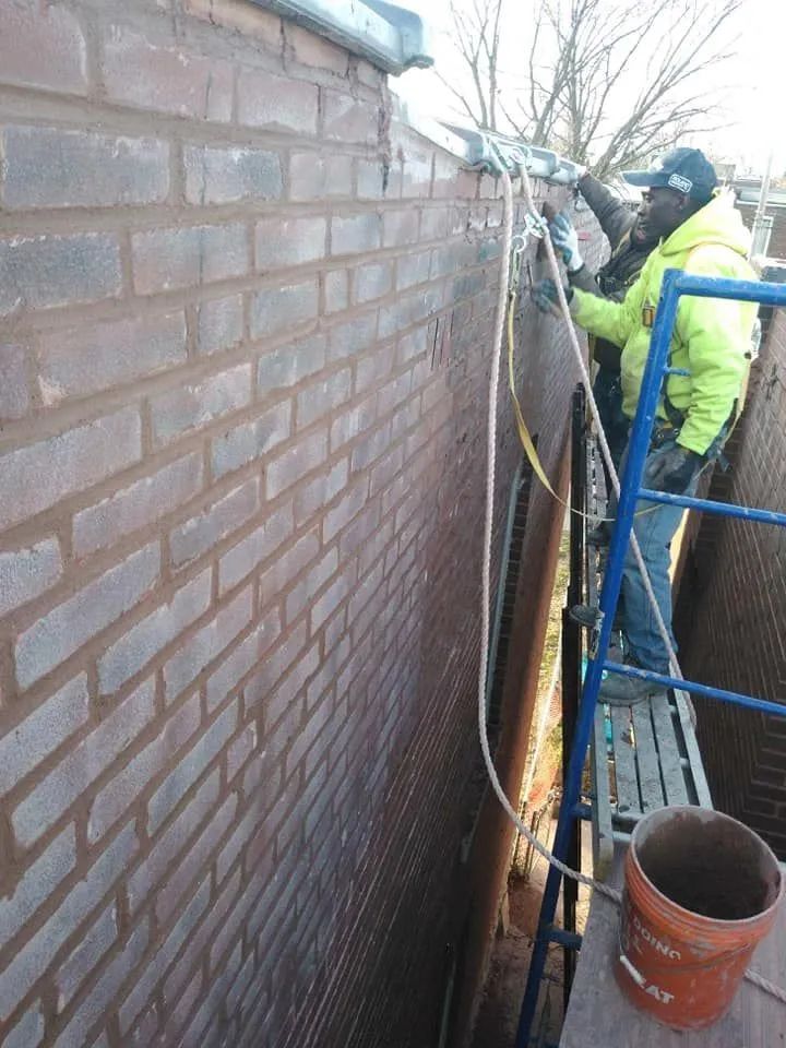 Worker on a blue ladder repairing a brick wall in a narrow outdoor space.