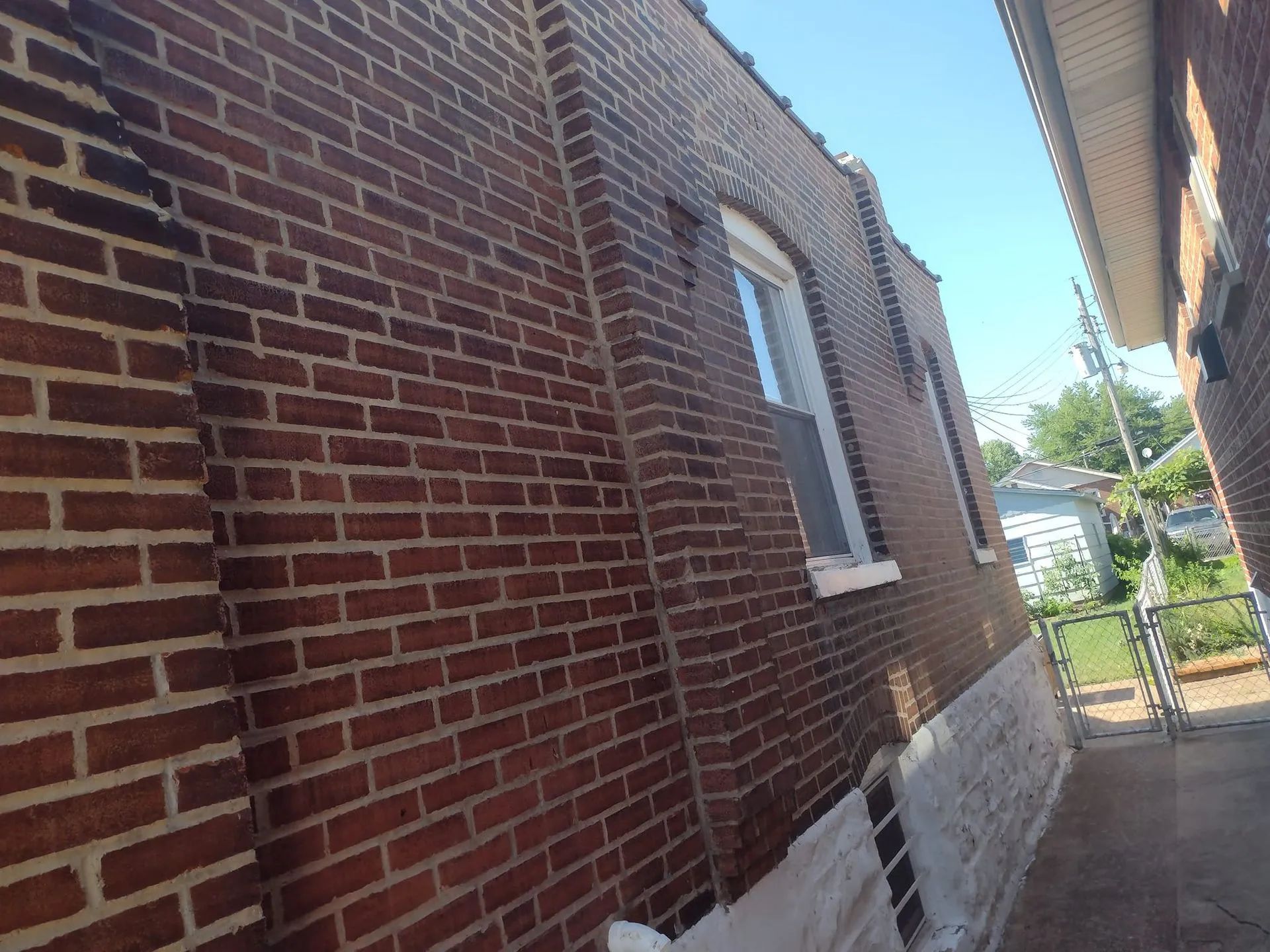Narrow alley beside a red brick building with white-trimmed windows and a stone foundation.