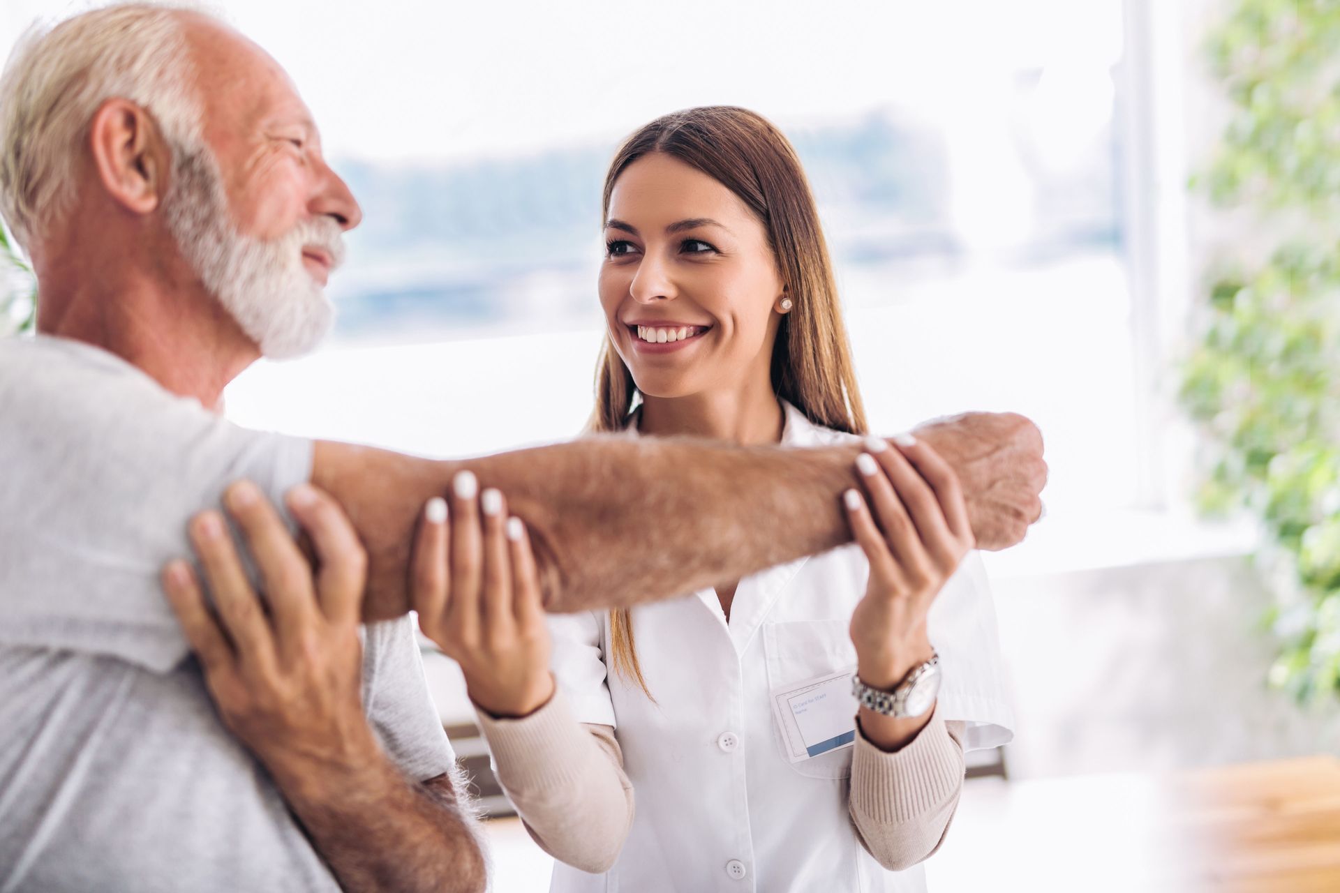 Doctor helping a smiling patient stretch his arm in a bright clinic
