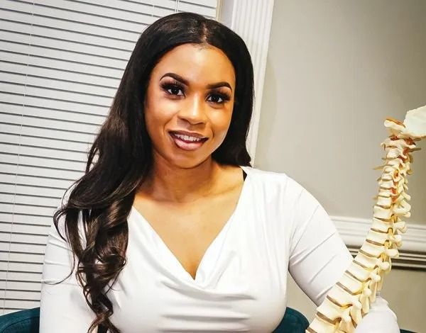 Woman in white top smiling beside a spine model in an office setting