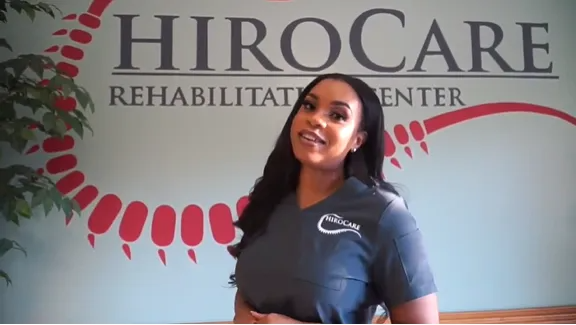 Woman standing in front of HIRoCARE Rehabilitation Center sign, smiling indoors