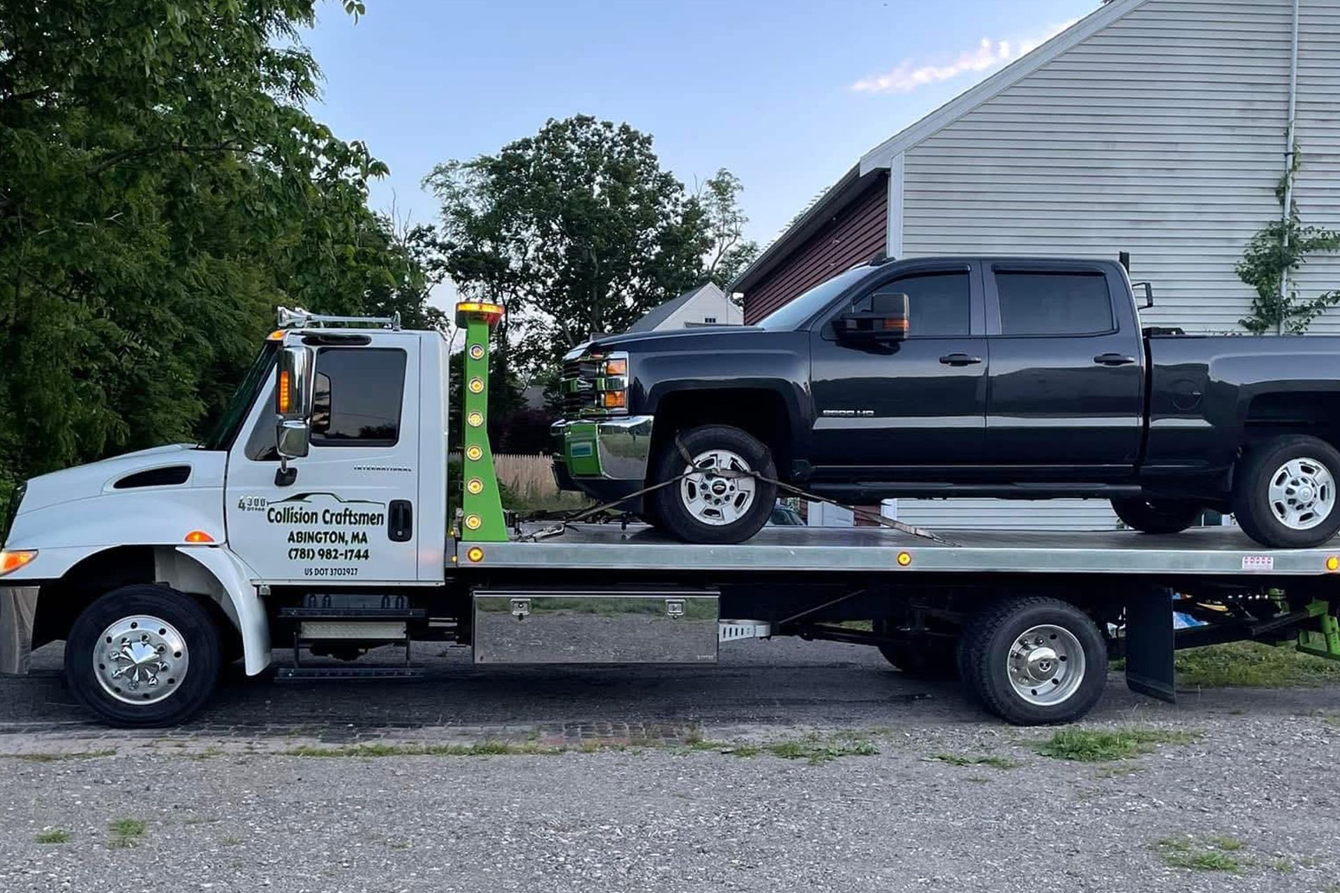 White tow truck carrying a black pickup truck on a flatbed. Outdoors, near a building.
