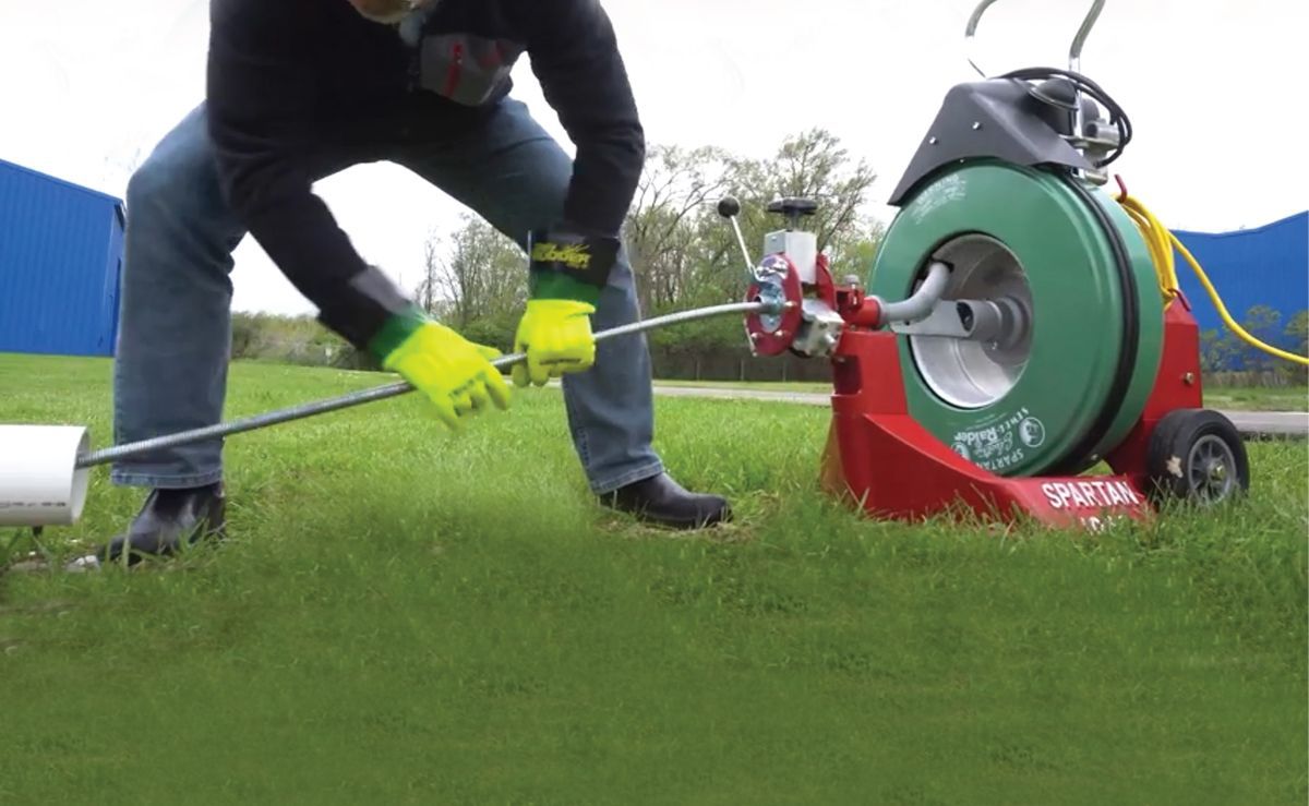 A man is using a drain cleaner on a lush green field.