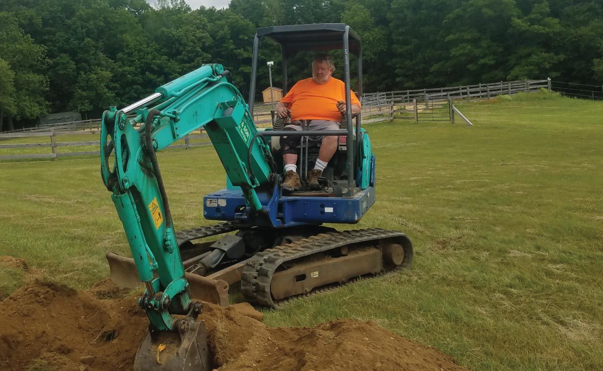 A man is driving a small excavator in a field.