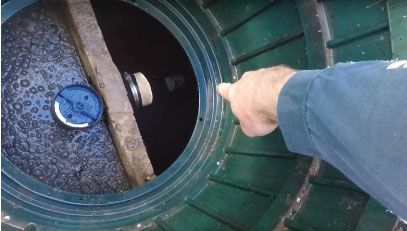 A person is pointing at a hole in a septic tank.