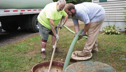 Two men are working on a septic tank in front of a truck.