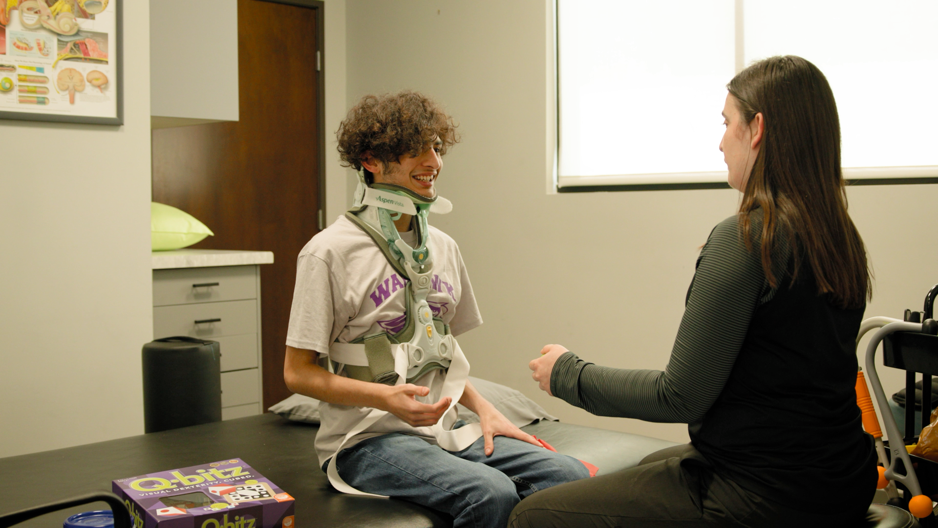 A woman is sitting next to a boy in a cast on a table.