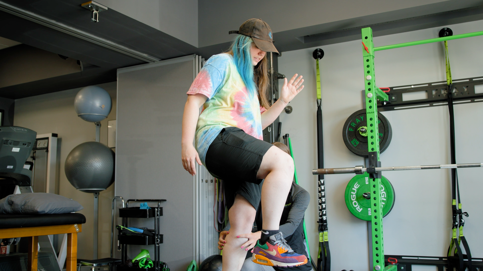 A woman with blue hair is standing on a ladder in a gym.