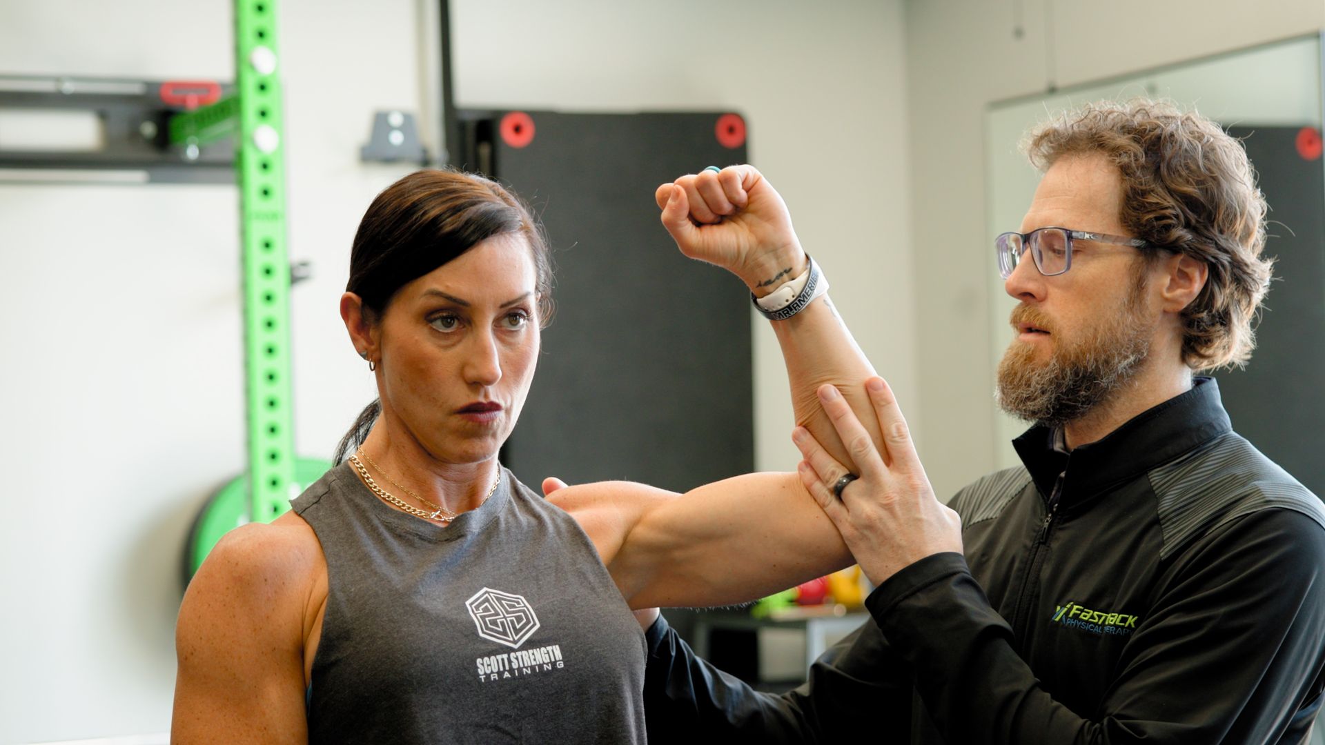 A man is examining a woman 's arm in a gym.
