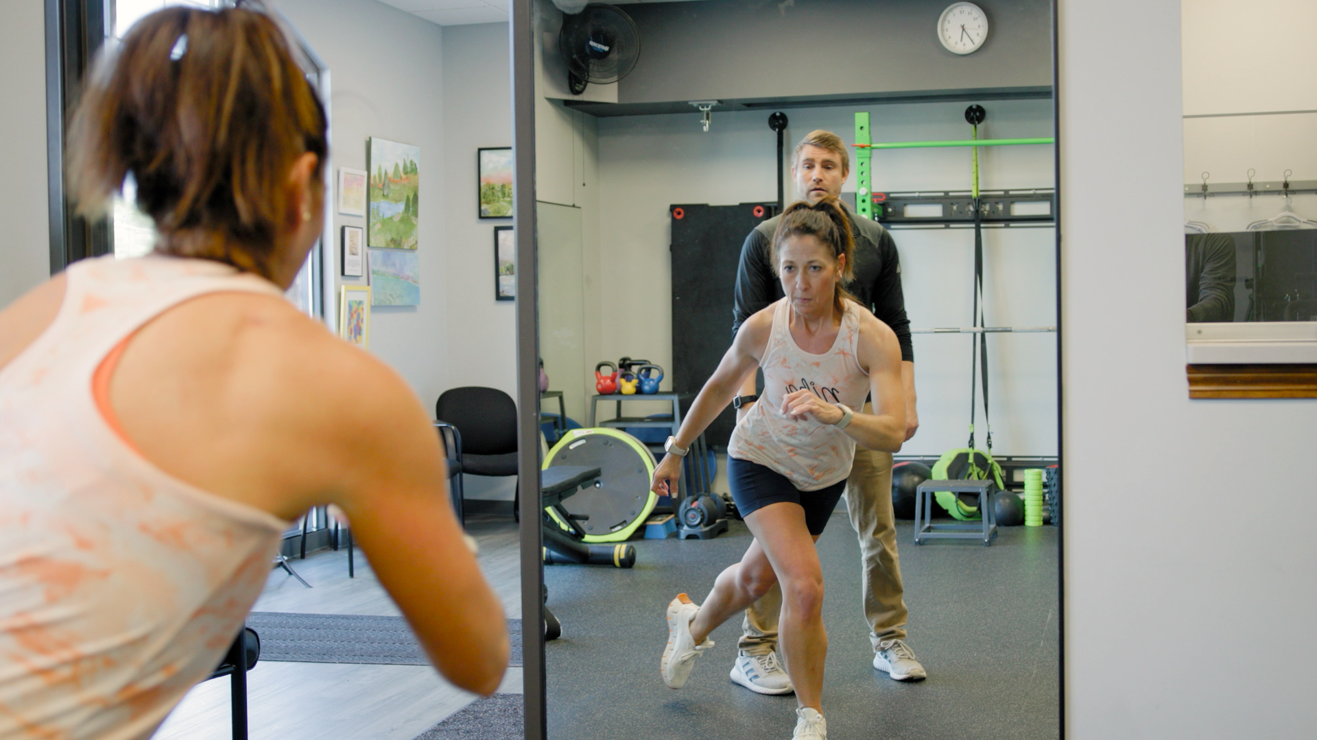 A woman is running in front of a mirror in a gym.