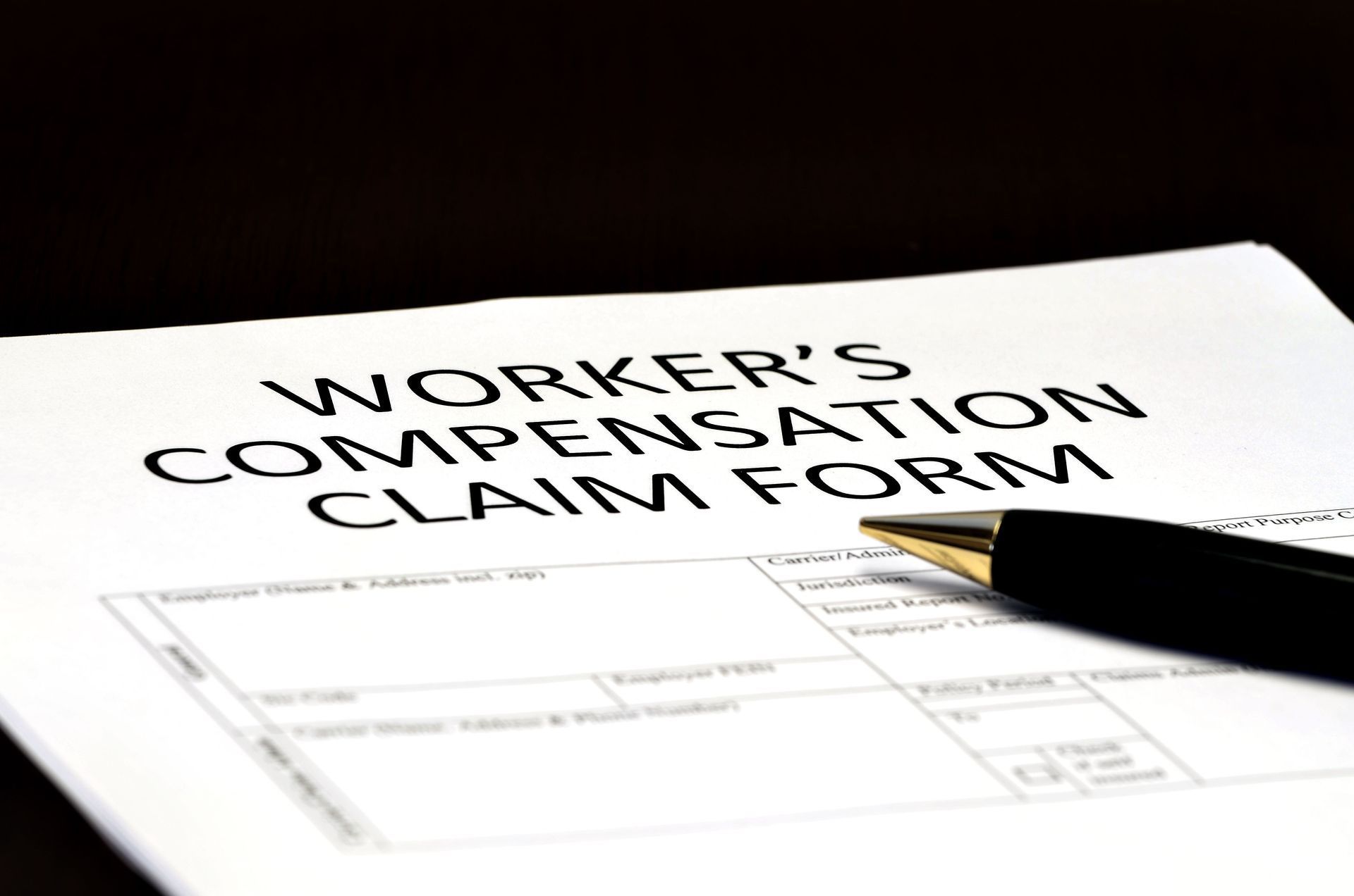 Worker's Compensation Claim Form with a pen on top. Black and white form on a dark surface.
