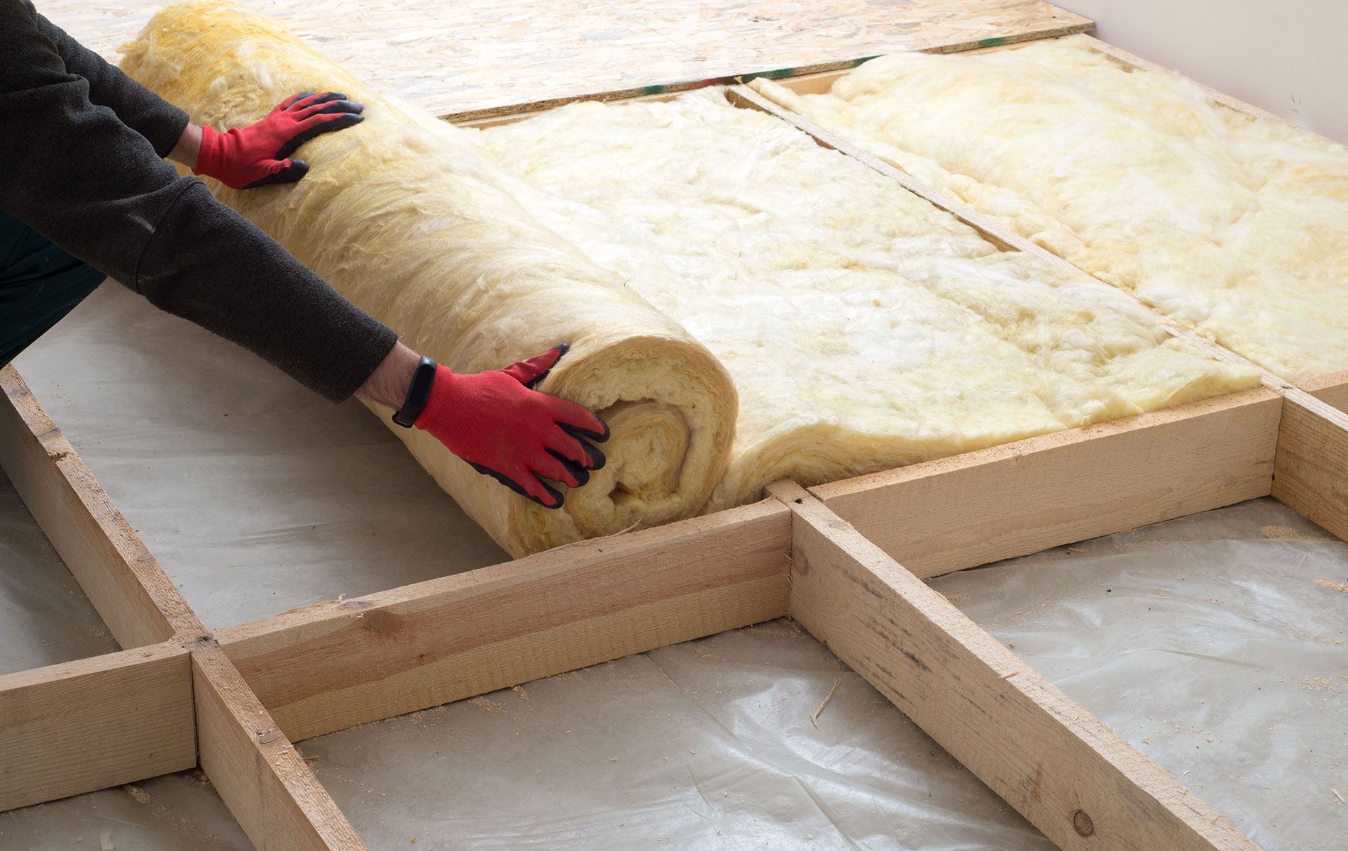 Person installing insulation rolls between wooden floor joists.