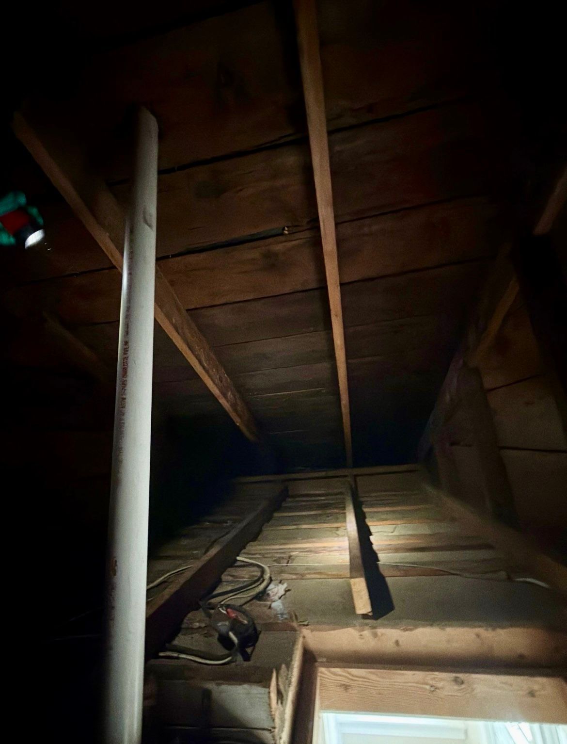 Dark attic space; wooden beams, white pipe, and exposed rafters.
