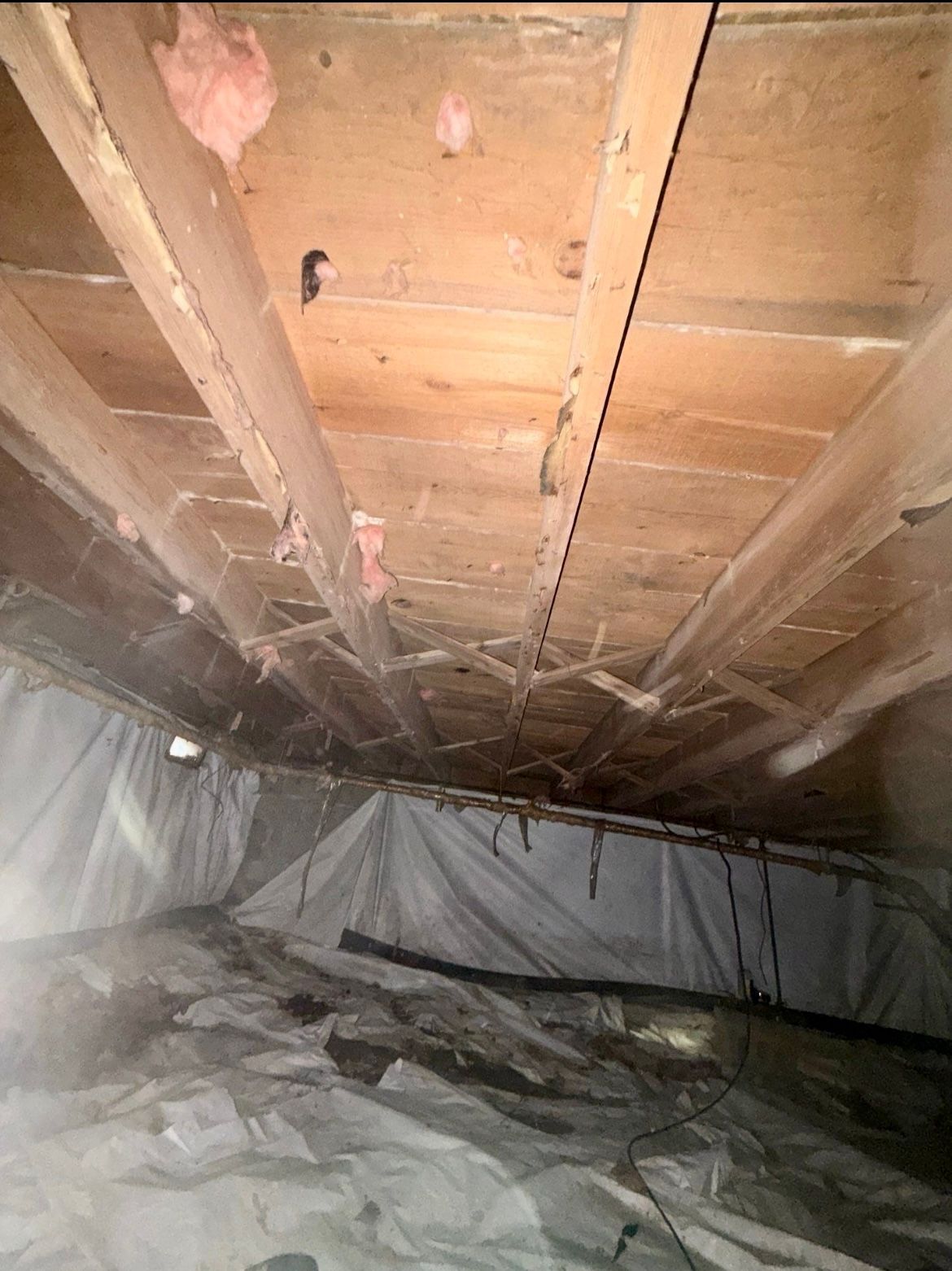 Interior crawl space with wood beams, insulation, and plastic sheeting.