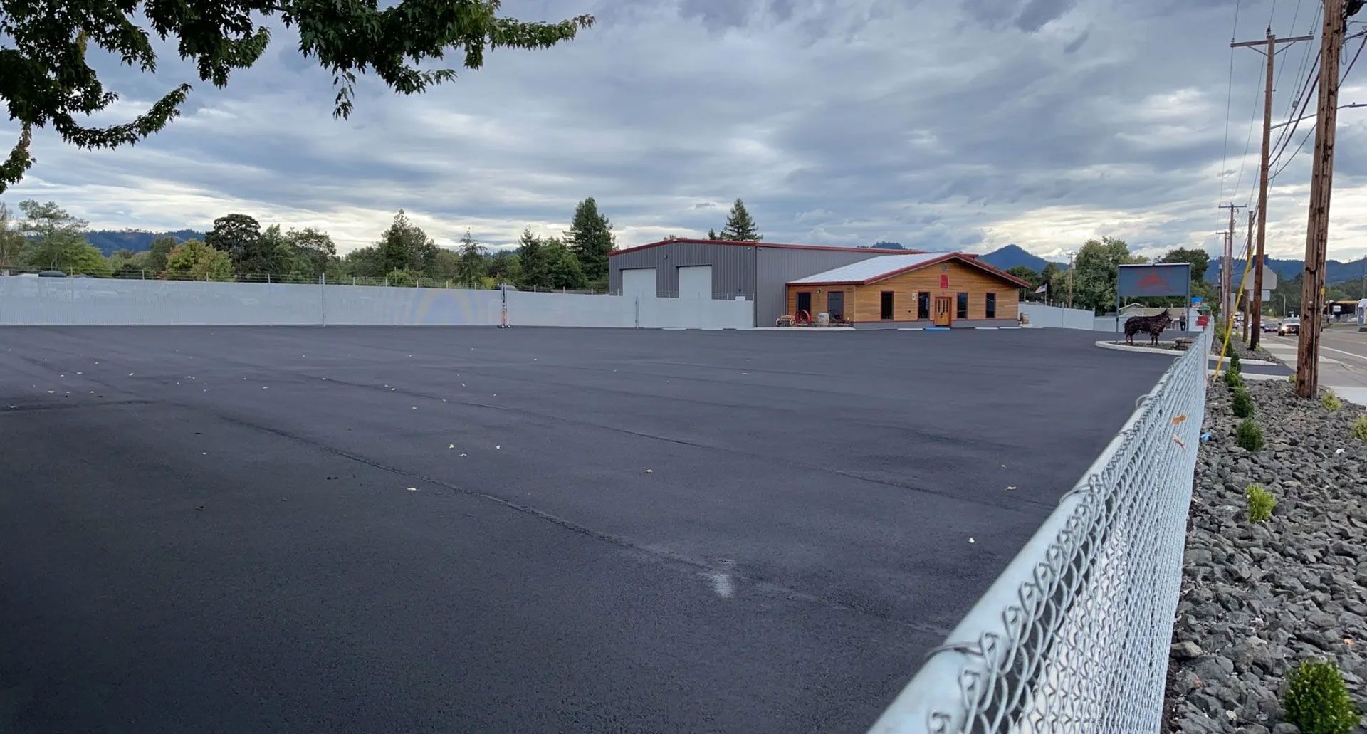 A large empty parking lot with a chain link fence and a building in the background.