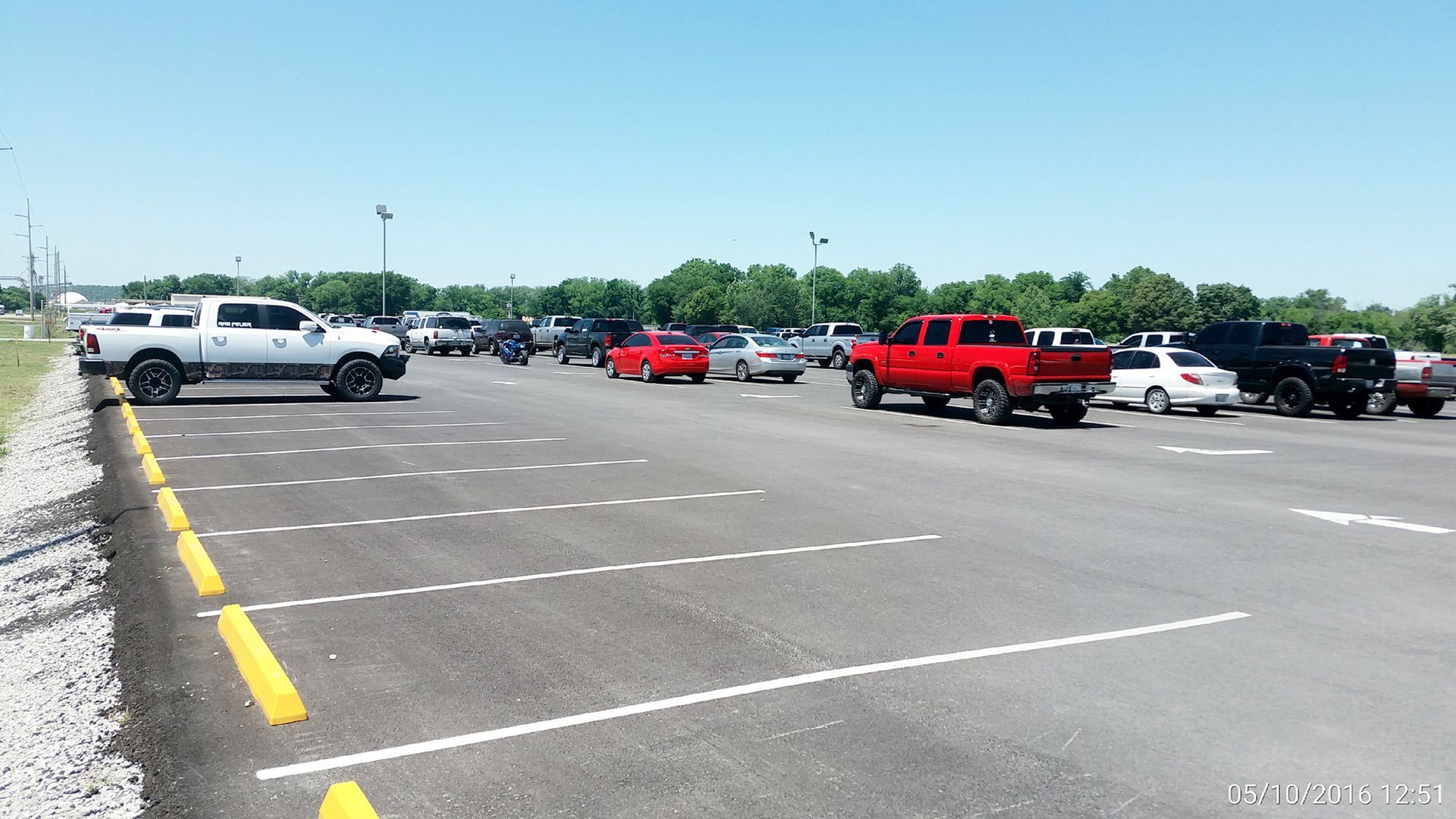 Mostly empty parking lot with several parked cars and trucks under a clear sky