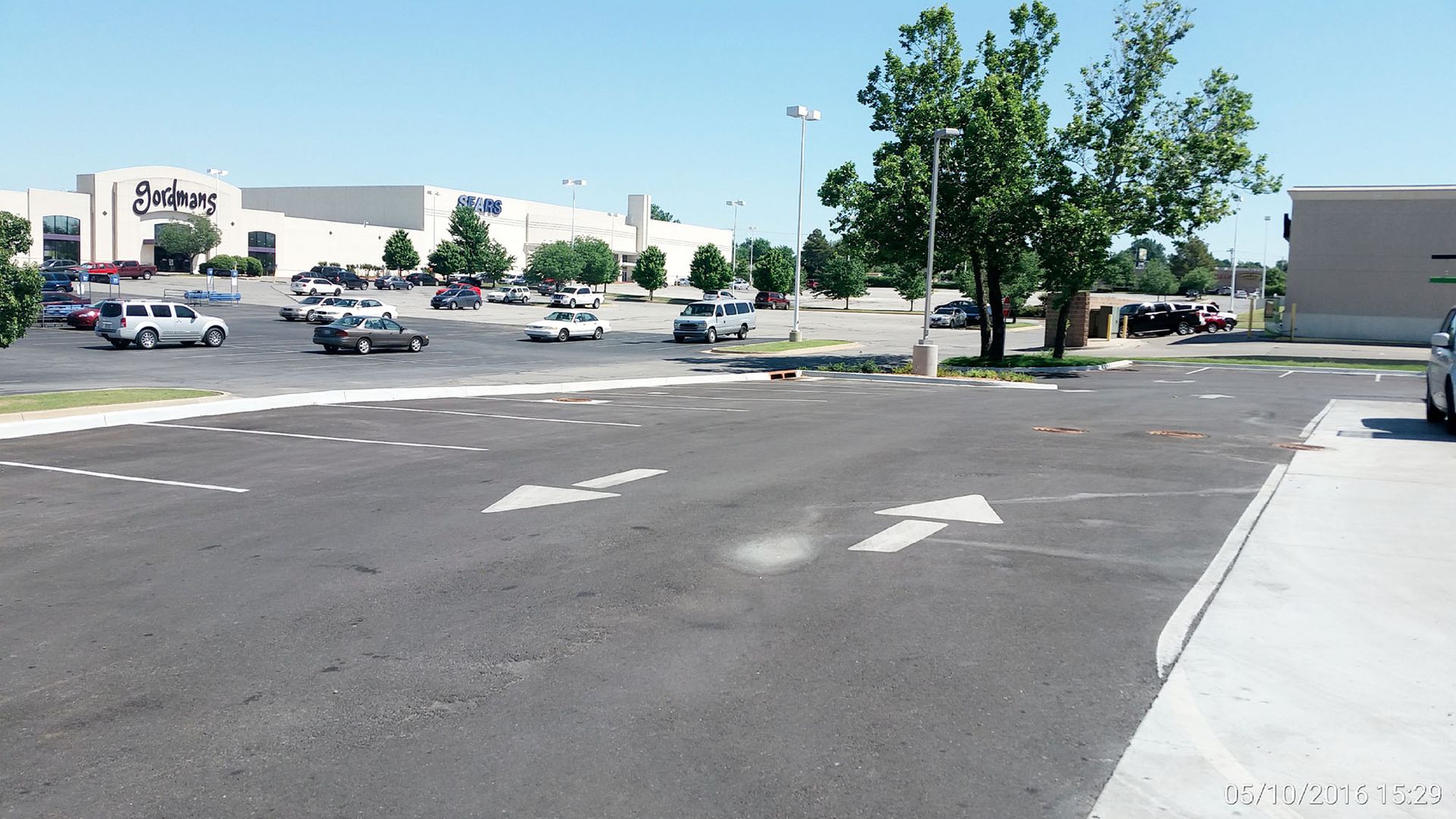 Walmart parking lot on a sunny day with scattered cars, trees, and empty asphalt in the foreground