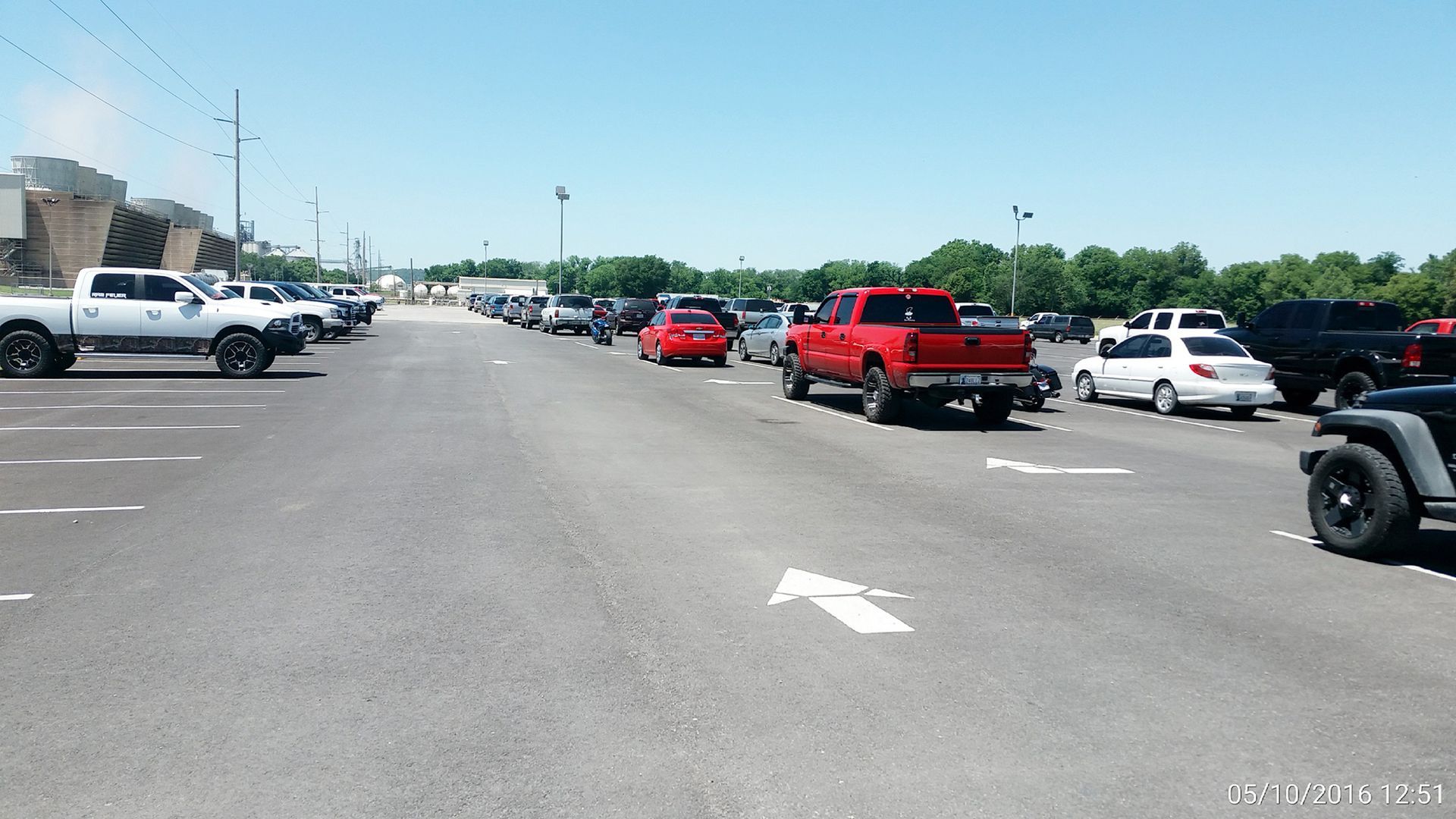 Cars lined up in a parking lot, including red pickups and white SUVs under a clear sky.